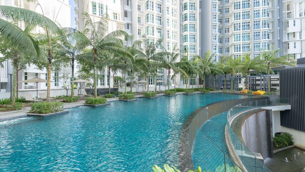 A swimming pool with a curved design, surrounded by palm trees and lounge chairs, set against a backdrop of modern high-rise buildings. - OYO Home 89736 Unbelievable 2br 1medini (Iskandar Puteri)
