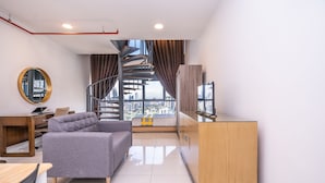Un salon moderne avec un canapé gris, un meuble en bois, une télévision et un escalier en colimaçon menant à un balcon offrant une vue sur la ville.