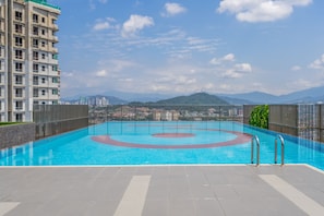 A rooftop swimming pool with a view of distant mountains and a high-rise building.