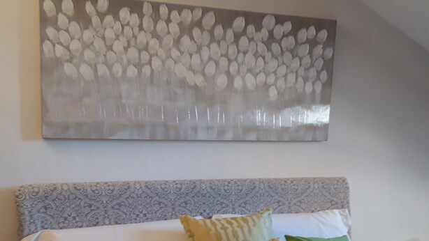 Un dormitorio con cama, almohadas y una obra de arte colgada en la pared.