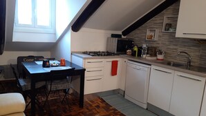 Una cocina compacta con gabinetes blancos, microondas, estufa a gas y un lavamanos. Hay una mesa de comedor con sillas y una alfombra en el suelo.