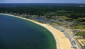 Luftaufnahme einer Küstenlandschaft mit Strand, einer Straße und mehreren Gebäuden.