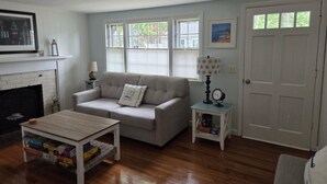 A living room with a fireplace, a sofa, a coffee table, and a side table with a lamp and clock. - ** Labor day on 3day min. Beach 0.7 Mi walk- Craigville & Covell. A/C, bikes. (Barnstable)