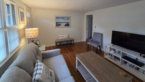 A living room with a sofa, a bench, a TV, and a lamp. - ** Labor day on 3day min. Beach 0.7 Mi walk- Craigville & Covell. A/C, bikes. (Barnstable)