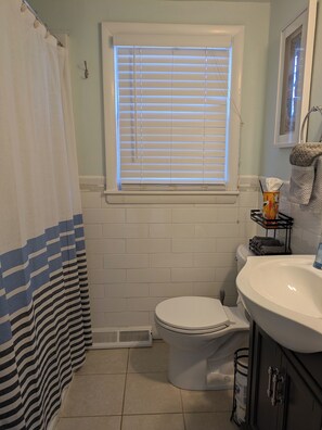 Ein Badezimmer mit Toilette, Waschbecken, einem Fenster mit Jalousien, einer Duschvorhang und einem Handtuchhalter.
