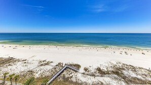 A beach with a wooden boardwalk leading to the shore, clear blue sky, and calm sea.