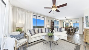 A spacious living room with a large sectional sofa, a round coffee table, and a ceiling fan.