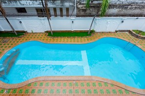 A swimming pool with a tiled edge, surrounded by a white wall with decorative elements and a fence topped with barbed wire.