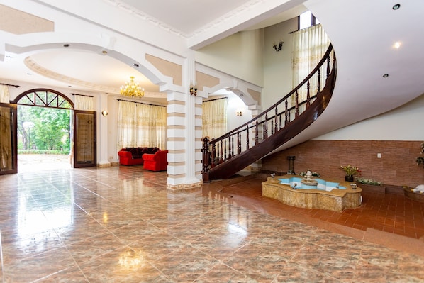 Un vestíbulo amplio con una escalera monumental, una fuente y asientos rojos.