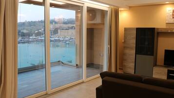 Un salon moderne doté d’une grande porte-fenêtre coulissante donnant sur un balcon avec vue sur un port de plaisance.