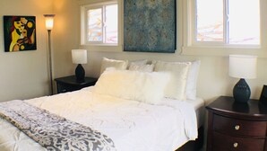 Un dormitorio con cama, dos mesitas de noche, una lámpara de pie y obras de arte en las paredes.