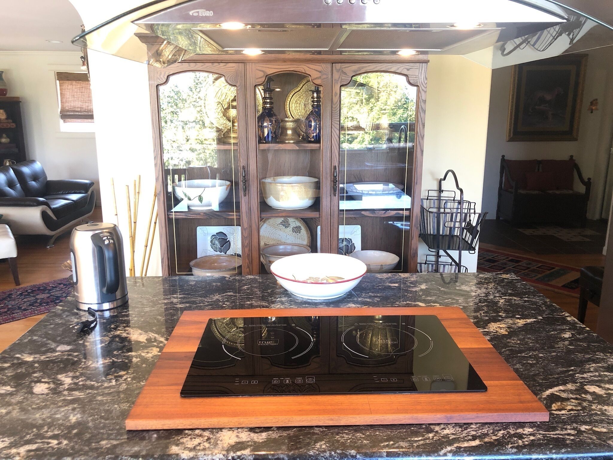 Une cuisine équipée d’une plaque de cuisson à induction, d’un meuble en bois avec des portes en verre et d’un coin repas comprenant une chaise et une table.