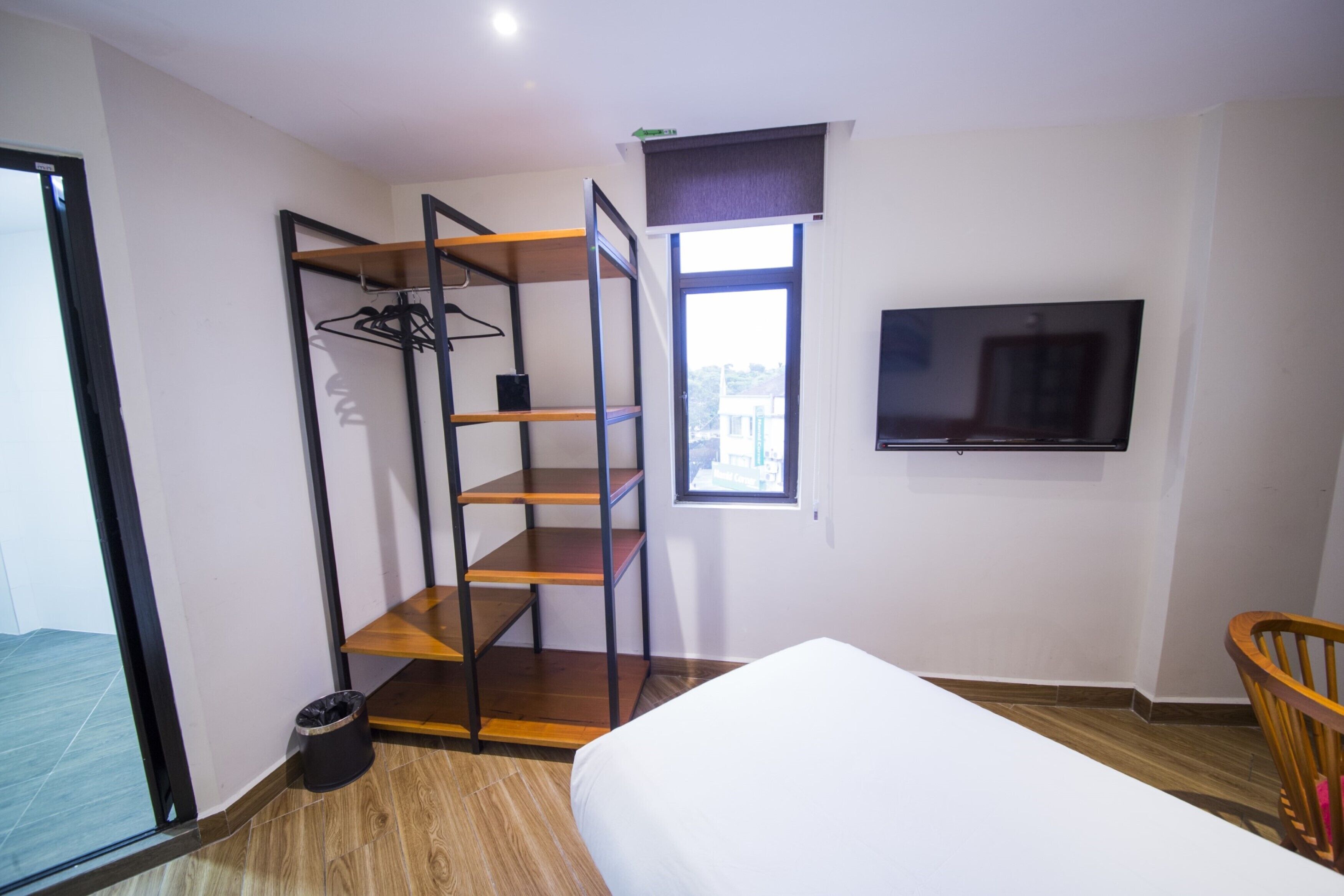 A bedroom with a bed, a TV, a window, a wooden chair, and a closet with shelves.