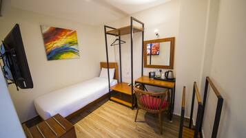 Habitación de hotel pequeña con una cama individual, un escritorio con silla, televisión y un cuadro en la pared.
