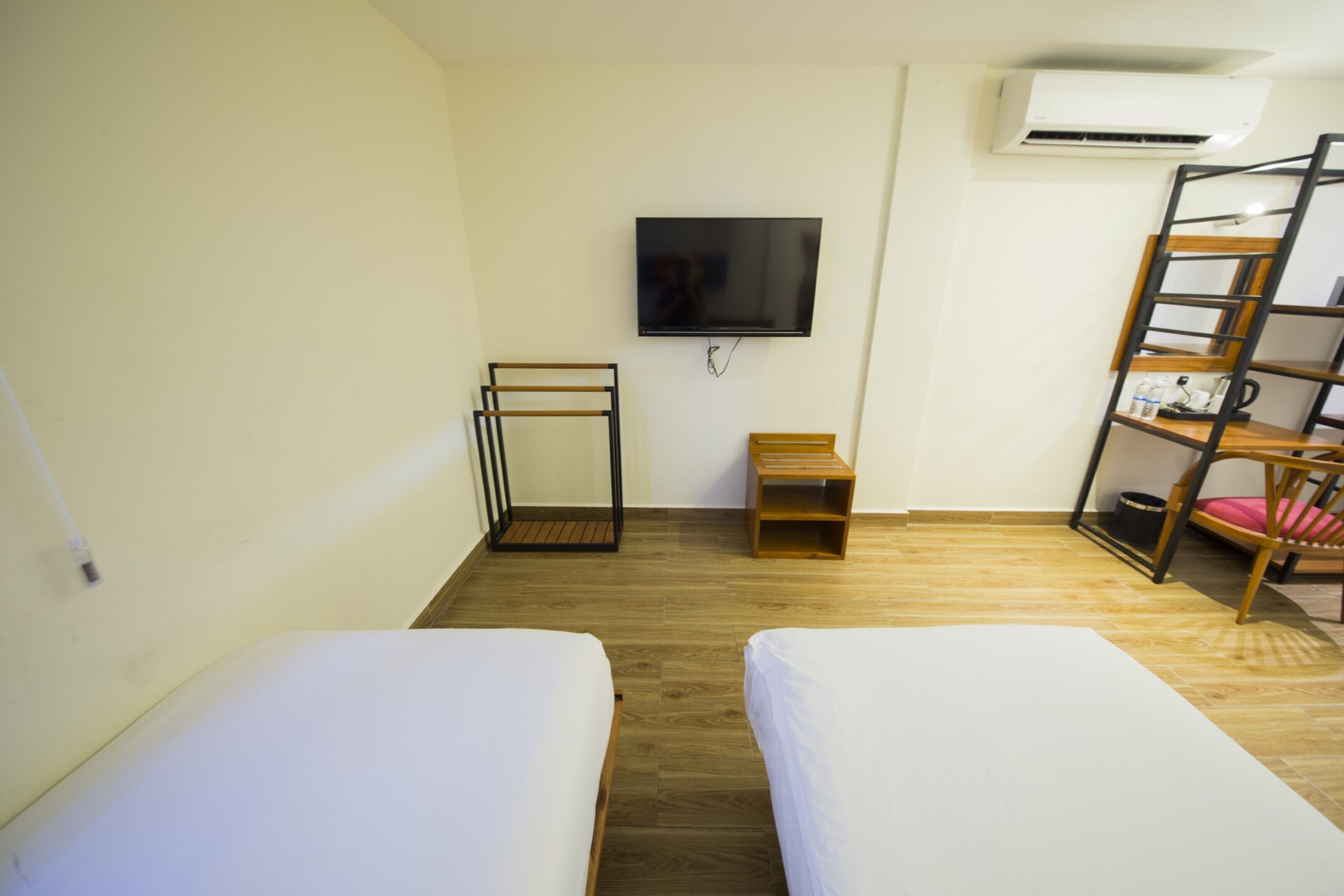 Ein Zimmer mit zwei Einzelbetten, einem an der Wand montierten Fernseher, Holzboden, einem kleinen Nachttisch aus Holz und einer Metallleiter an der Wand.
