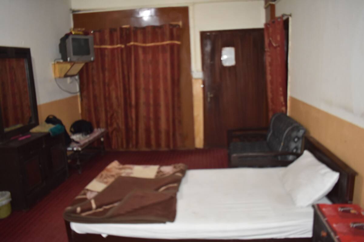 A room with a bed, a desk, a chair, a television on a shelf, and a door.