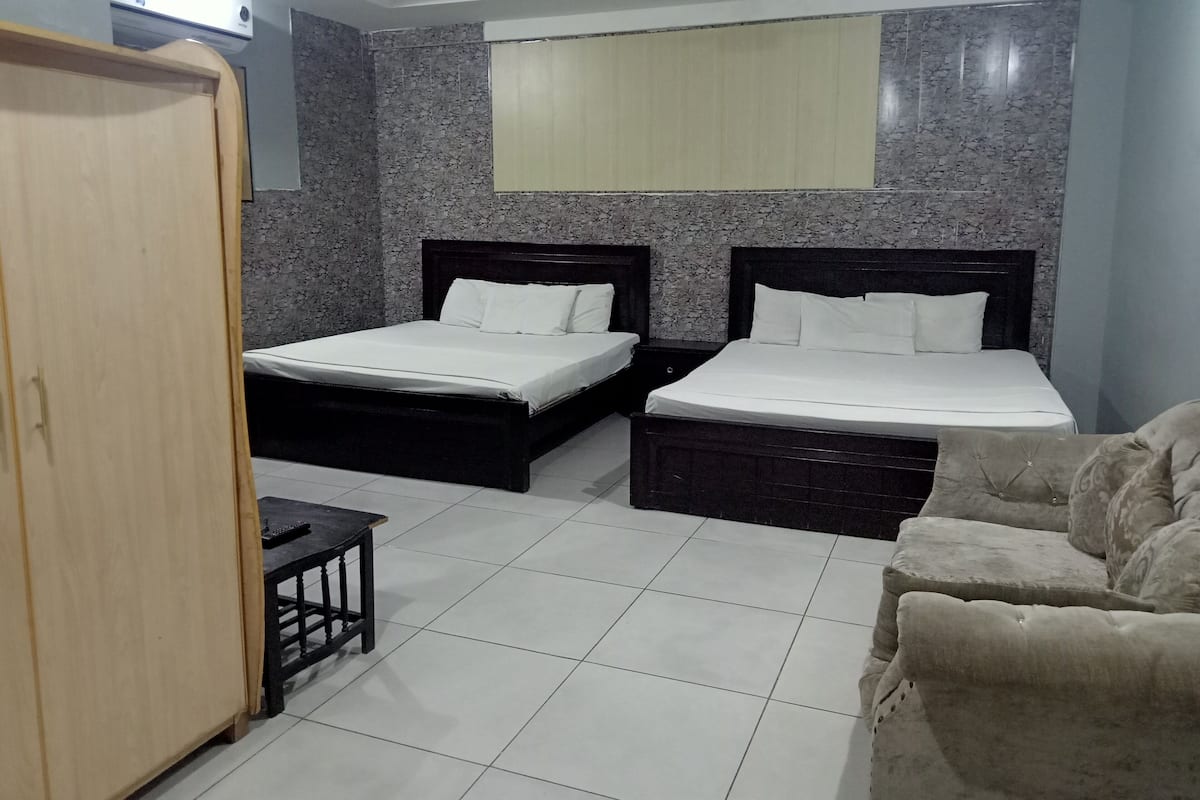 A hotel room with two beds, a wardrobe, a small table, and a sofa.