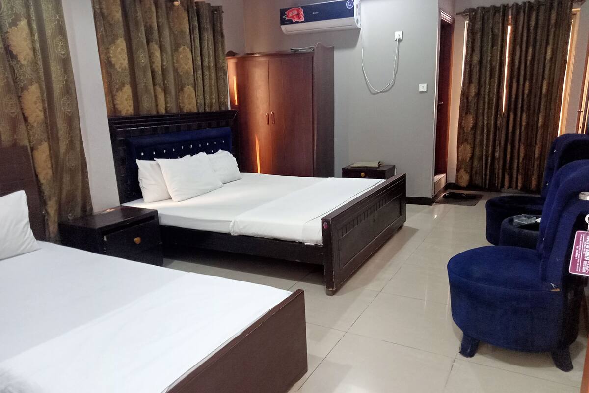 A hotel room with two beds, a wardrobe, a chair, and a small table.