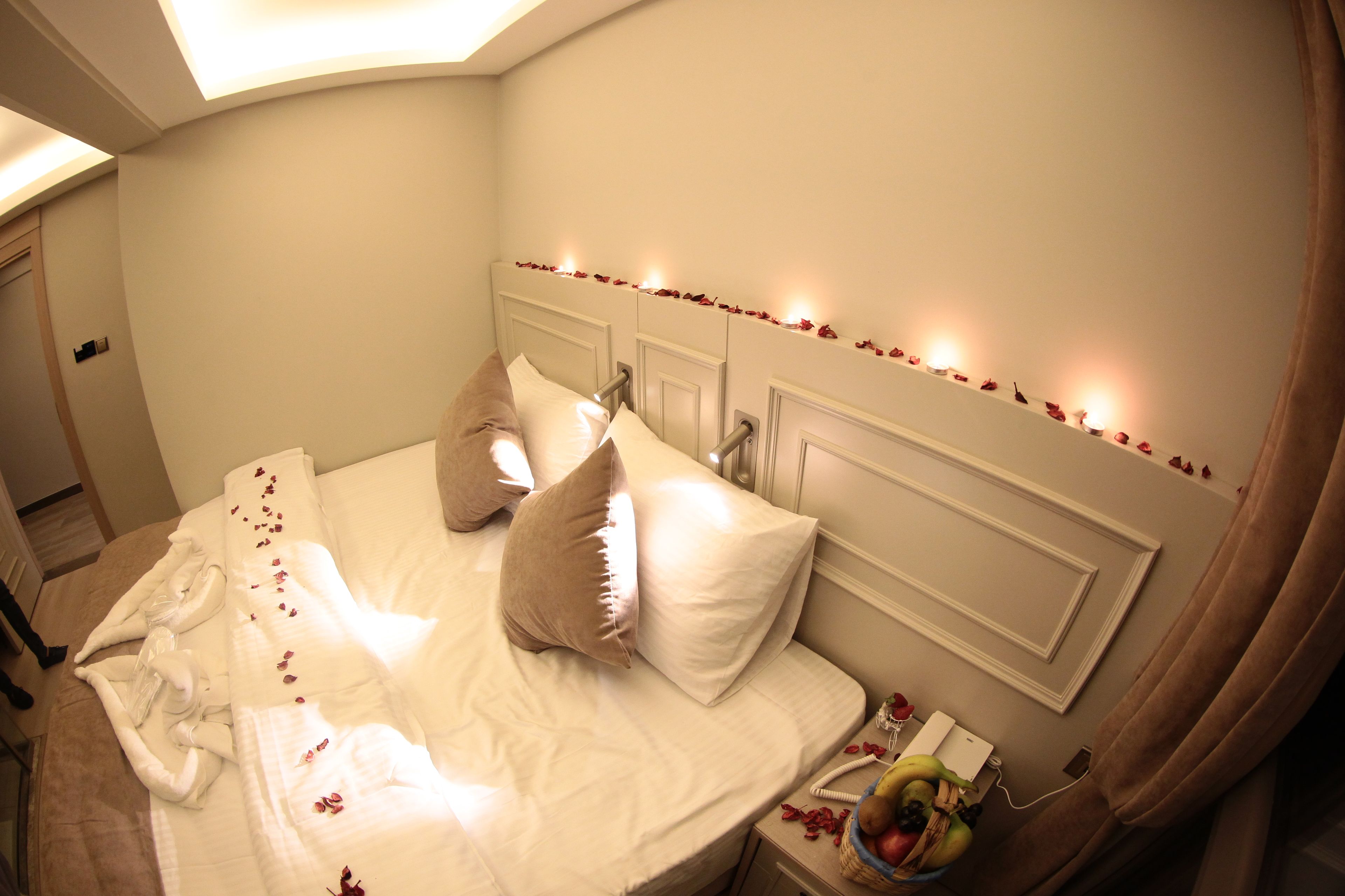 Ein ordentlich bezogenes Bett mit Kissen, ein Nachttisch mit Obstschale und ein Beistelltischchen mit Lampe.
