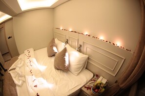 A neatly made bed with pillows, a bedside table with a fruit bowl, and a nightstand with a lamp. - X-Nellyi Boutique Hotel (Istanbul)