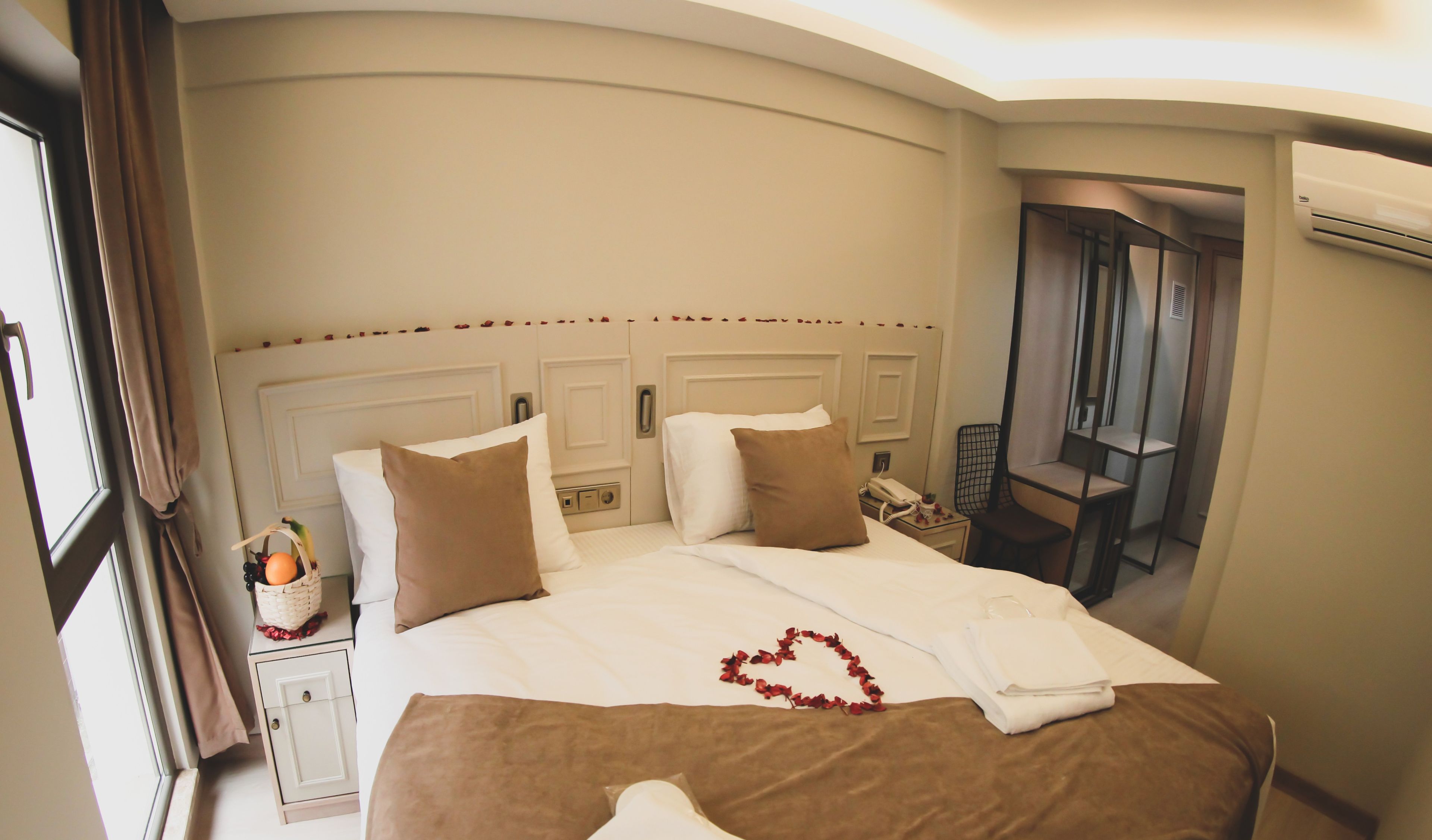 Una habitación de hotel con una cama grande, una mesita de noche con lámpara, una silla y un aire acondicionado.