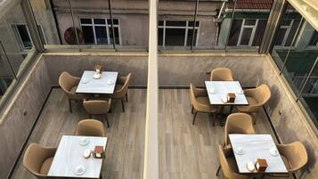 Un espace de restauration aménagé sur le toit, avec des tables et des chaises, offrant une vue sur la façade de l’immeuble et un ciel dégagé.