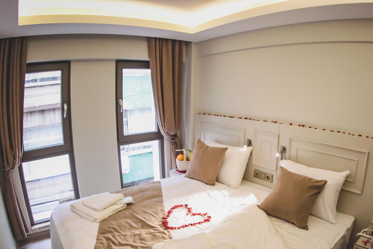 Quarto de hotel com uma cama, mesa de cabeceira e telefone, e uma janela com cortinas.