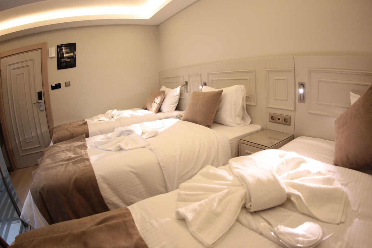 Quarto de hotel com duas camas, uma mesinha de cabeceira e um aquecedor fixado na parede.