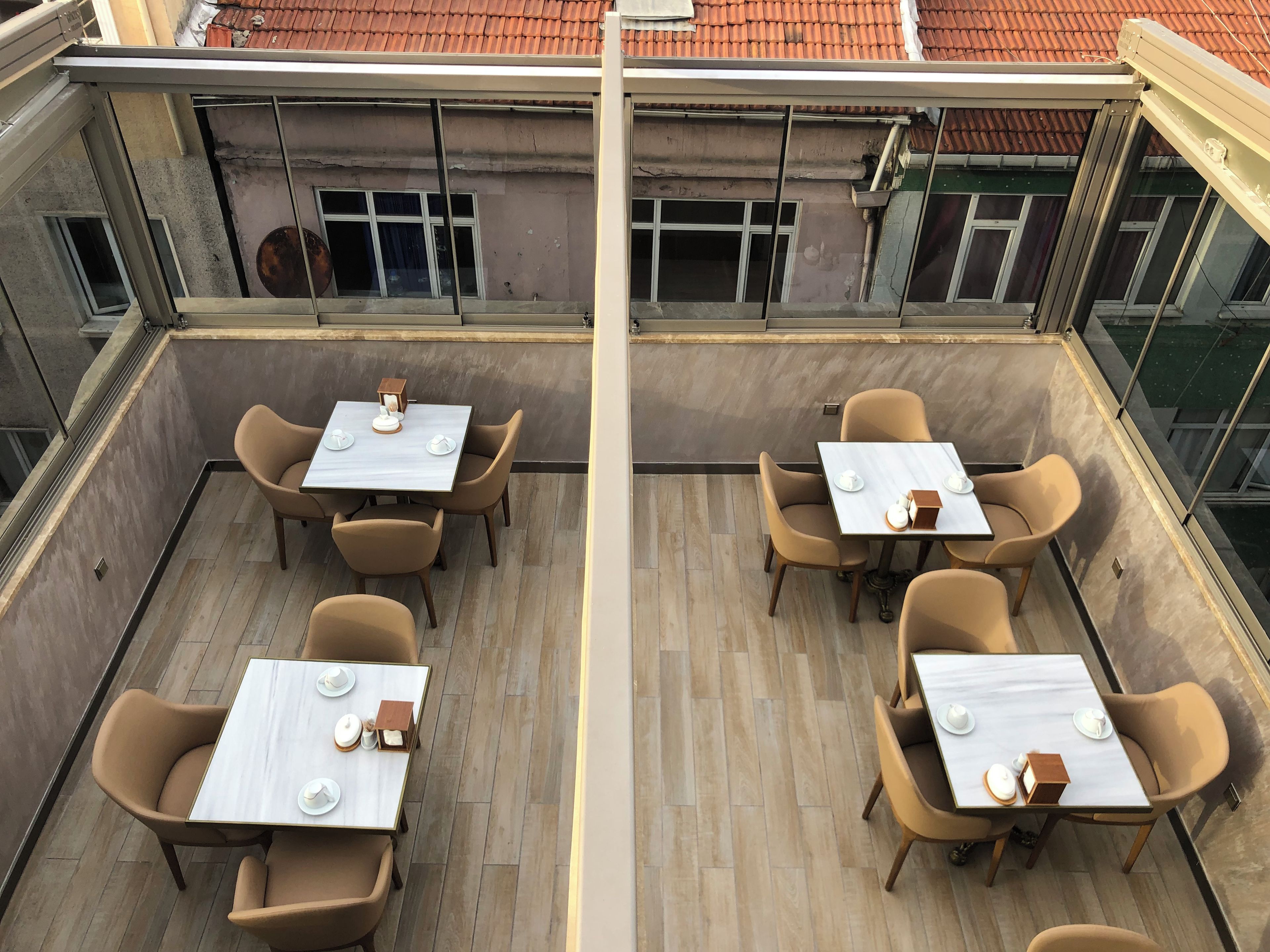 A rooftop dining area with tables and chairs, a view of the building's exterior, and a clear sky.