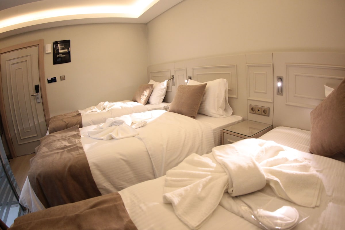 A hotel room with two beds, a bedside table, and a wall-mounted heater.