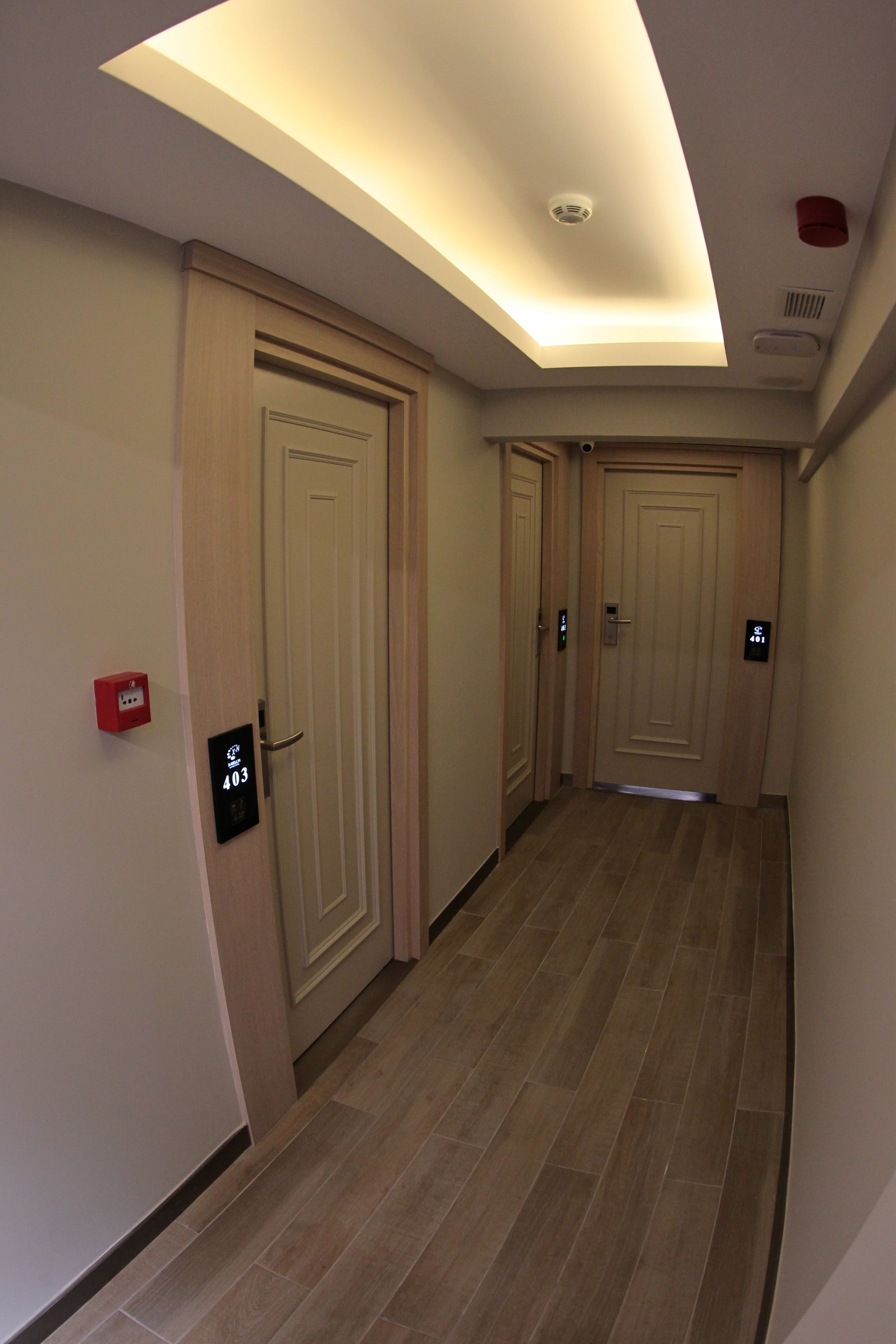 A hotel corridor with wooden doors, a red emergency phone, and a ceiling light.