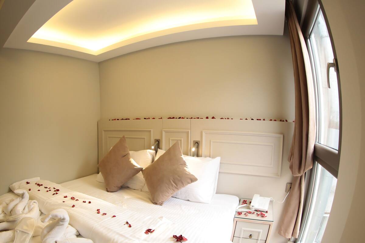 A hotel room with a bed, a bedside table with a phone, and a window with curtains.