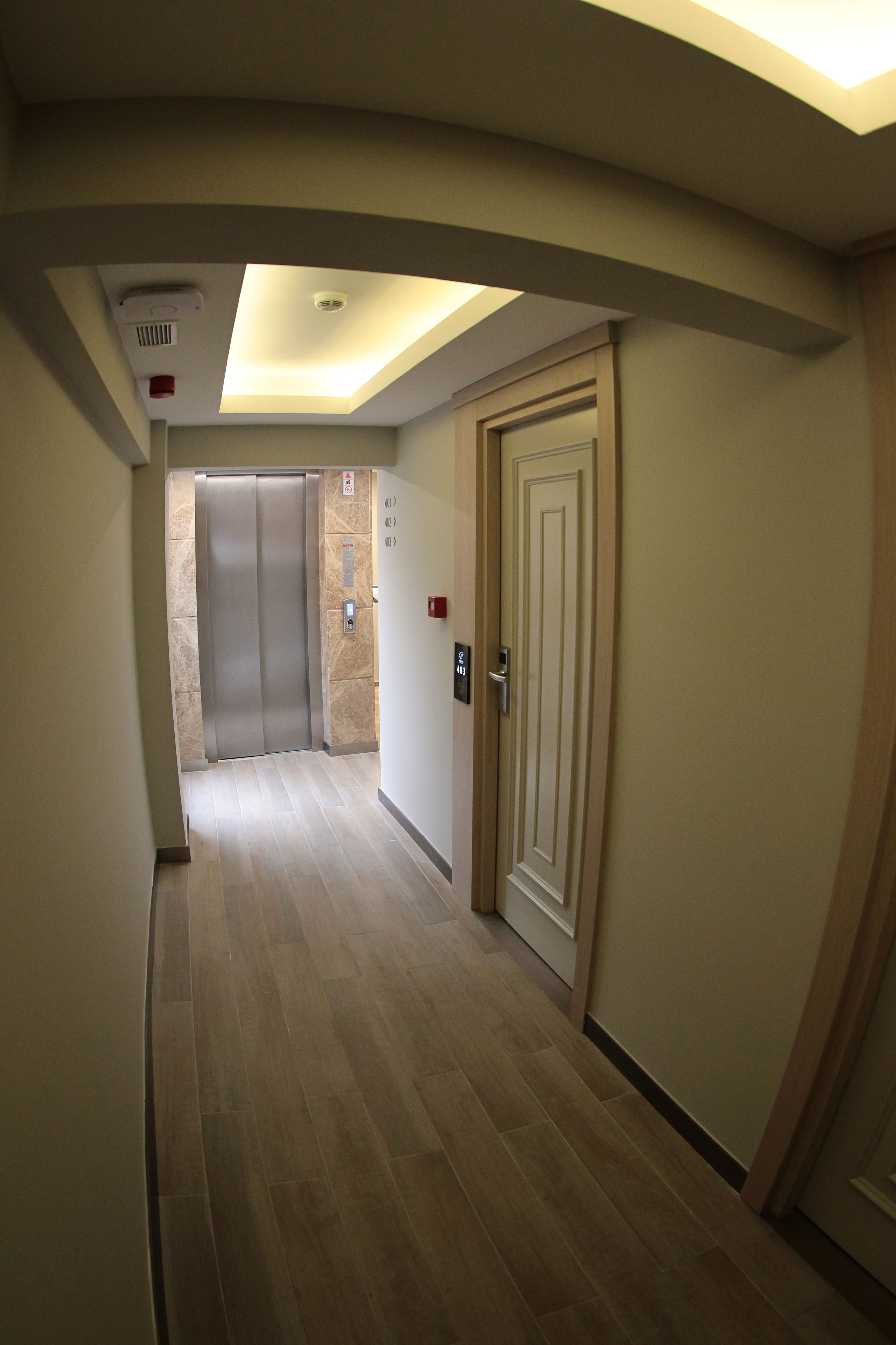 A corridor with a ceiling light, an elevator, and a door with a number plate.