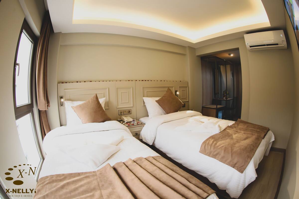 A hotel room with two beds, a nightstand, and an air conditioning unit.