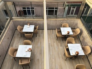 Un espace de restauration aménagé sur le toit, avec des tables et des chaises, offrant une vue sur la façade de l’immeuble et doté d’une rambarde en verre.