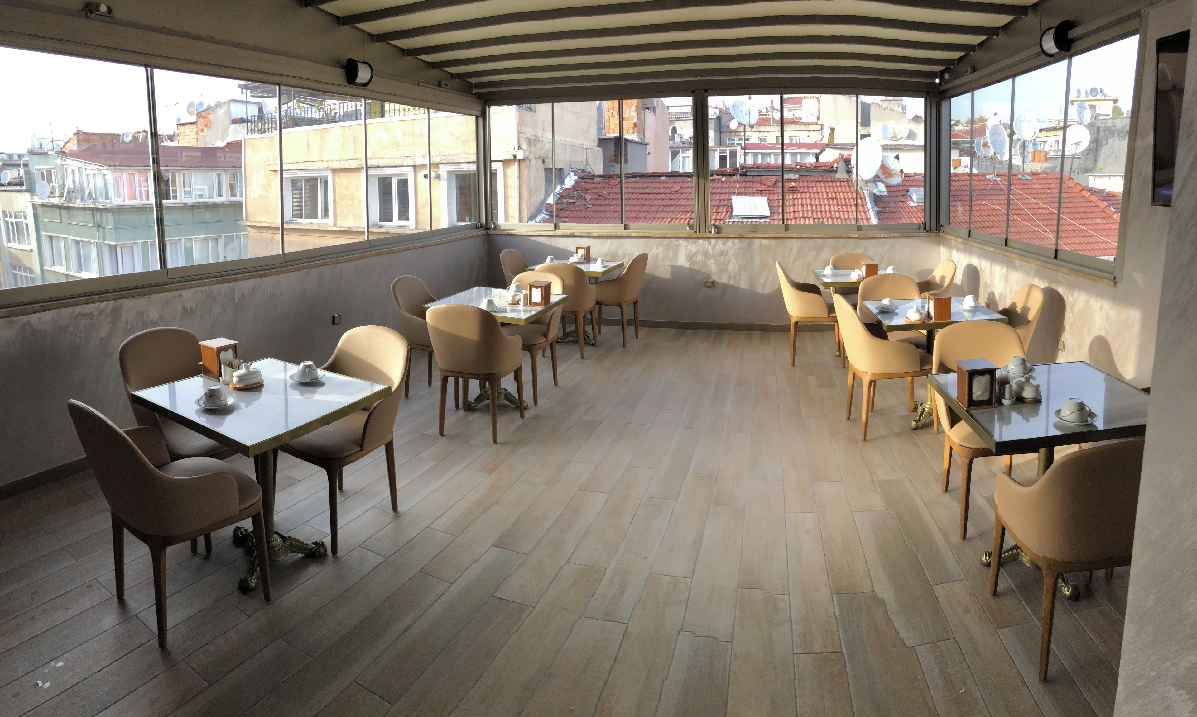 Un espace de restauration aménagé sur le toit, avec plusieurs tables et chaises, et de grandes fenêtres offrant une vue sur le paysage urbain.