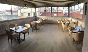 A rooftop dining area with multiple tables and chairs, large windows offering a view of the cityscape. - X-Nellyi Boutique Hotel (Istanbul)