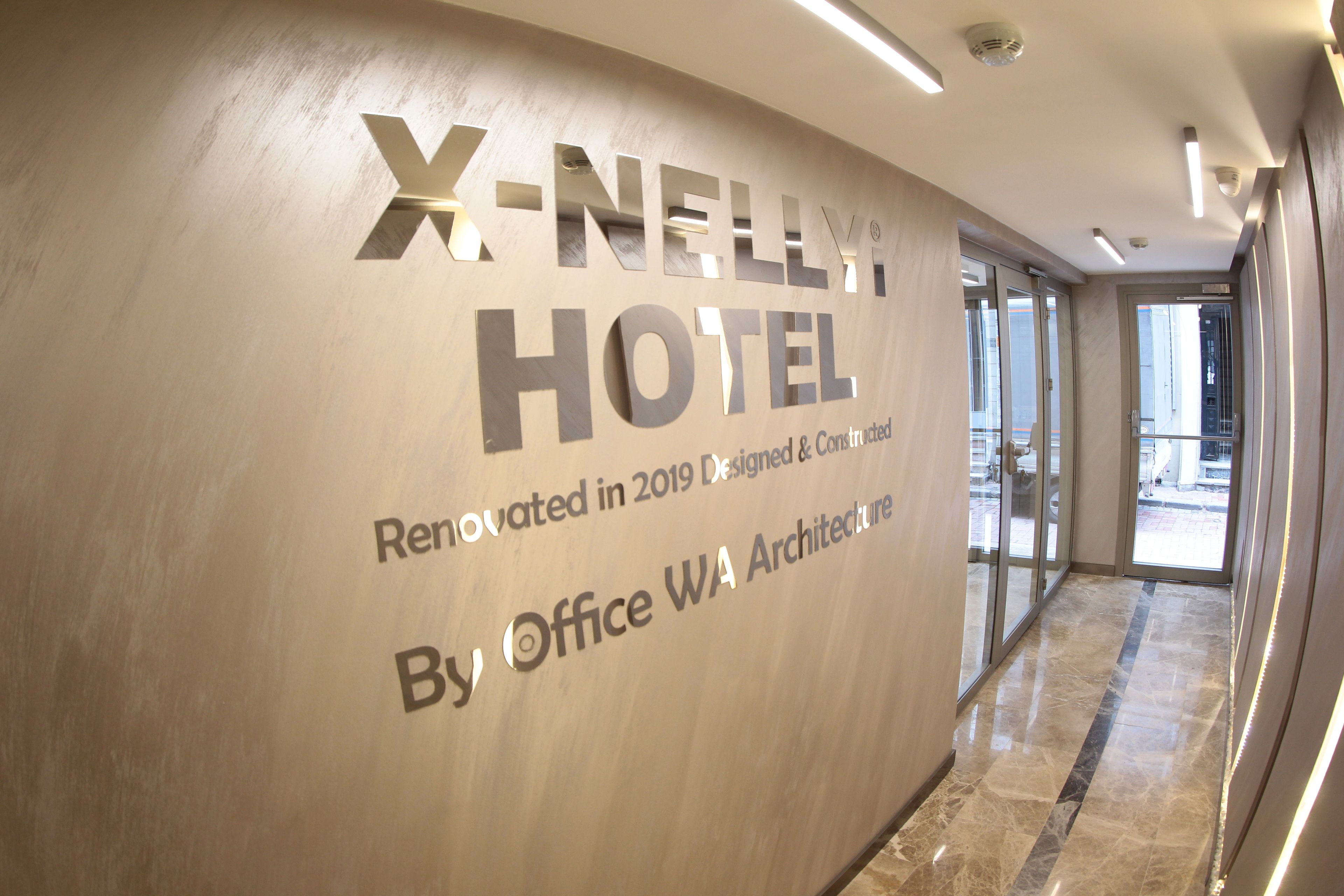 A hallway with a wall displaying the text 'X-NELL HOTEL' and 'Renovated in 2019 Designed & Constructed by Office WA Architecture.'