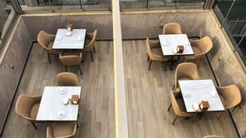 A rooftop terrace with tables and chairs, a view of the cityscape, and a glass railing.