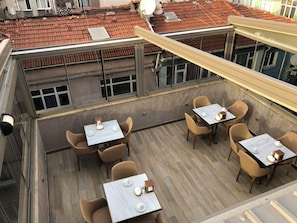 Een dak terras met meerdere tafels en stoelen, een uitzicht op de stads skyline, en een rood pannendak.