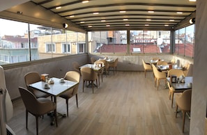 A rooftop restaurant with tables and chairs, large windows, and a view of buildings. - X-NELLYİ HOTEL (Istanbul)