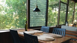 Een eetruimte met een houten tafel, zwarte stoelen, geweven placemats en een hangende hanglamp.