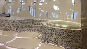 A spa area with a mosaic-tiled jacuzzi, stone steps, and a wall with cut-out patterns. - Luton Vacation Homes Damac Heights (Dubai)