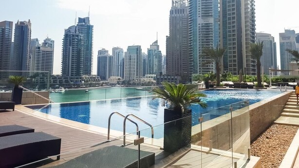 A rooftop pool with a city skyline view, surrounded by lounge areas and a clear sky. - Luton Vacation Homes Damac Heights (Dubai)