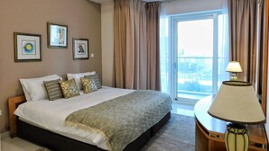A hotel room with a large bed, a nightstand with a lamp, a window with curtains, and two framed pictures on the wall. - Luton Vacation Homes Damac Heights (Dubai)