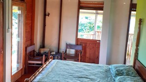 Un dormitorio con una cama de madera, una silla y una mesita pequeña. Hay una puerta que da a un balcón.