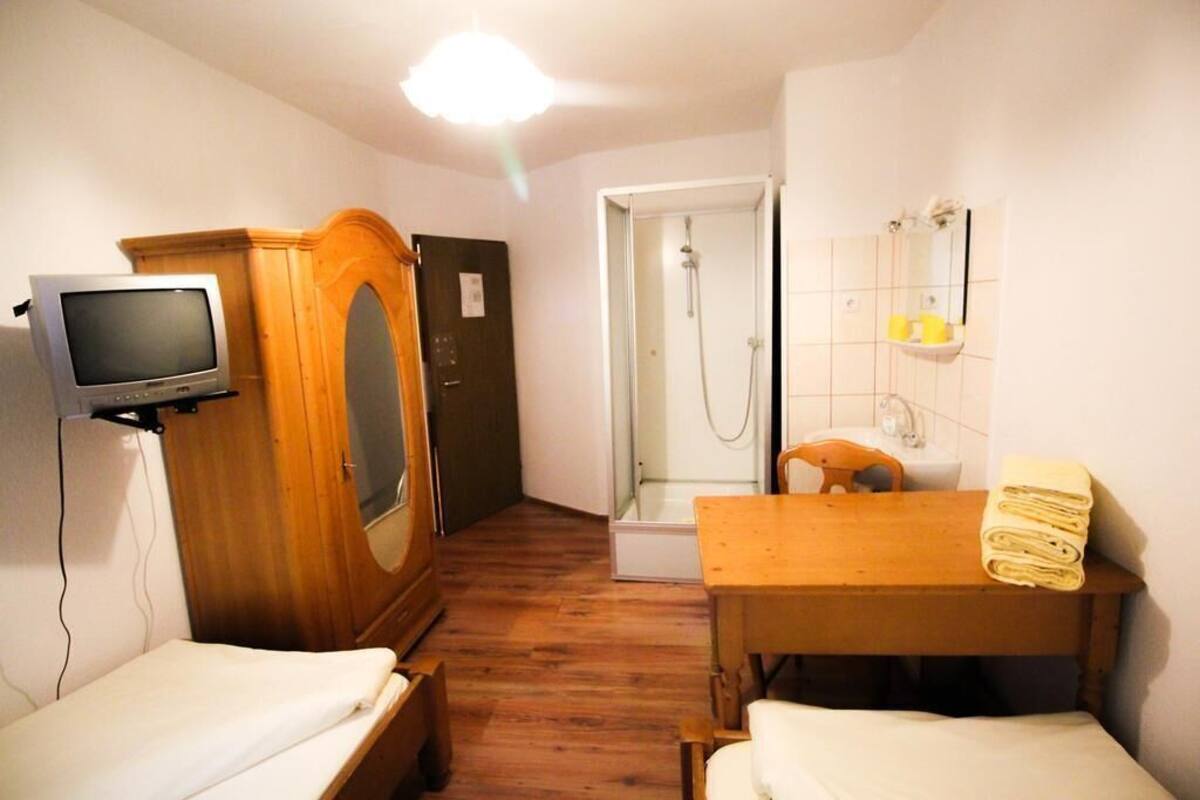 Une petite pièce comprenant une armoire en bois, une télévision, une douche, une table avec une serviette et un lit.