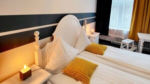 Une chambre d’hôtel avec deux lits, une table de chevet avec une lampe, une petite table et une fenêtre avec des rideaux.