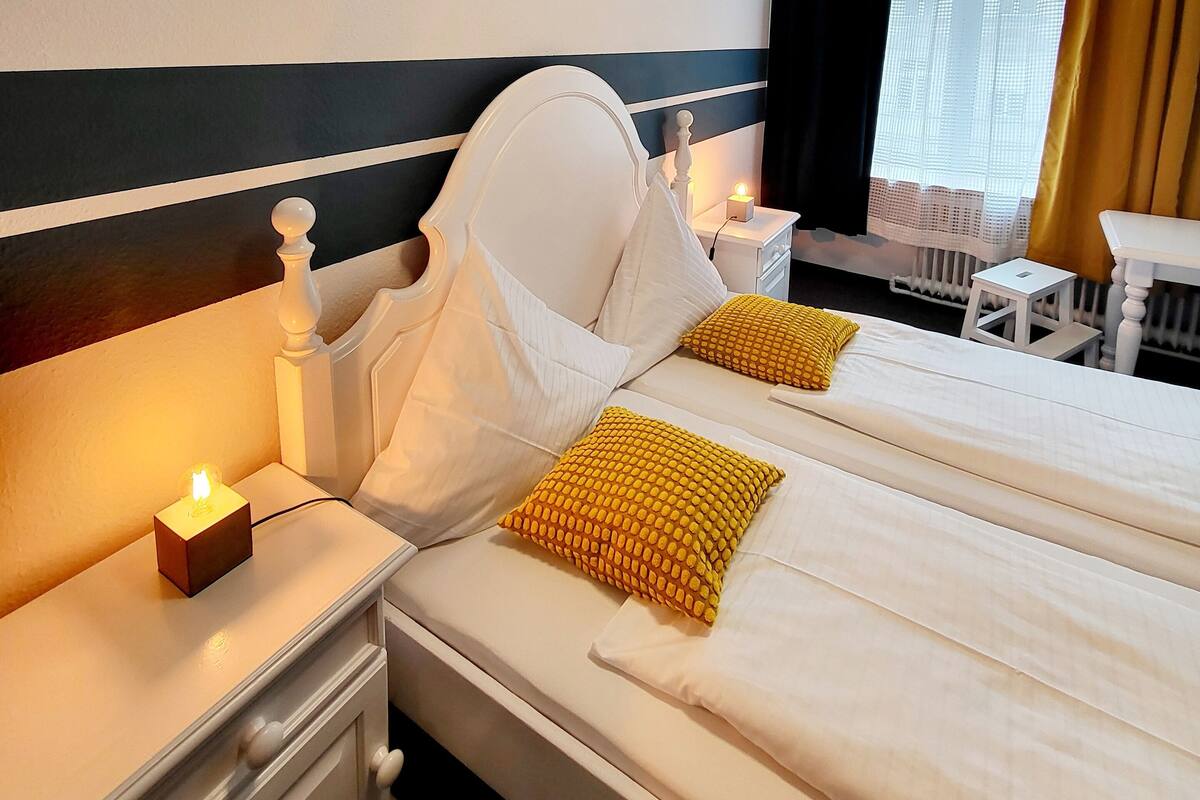 Une chambre d’hôtel avec deux lits, une table de chevet avec une lampe, une petite table et une fenêtre avec des rideaux.