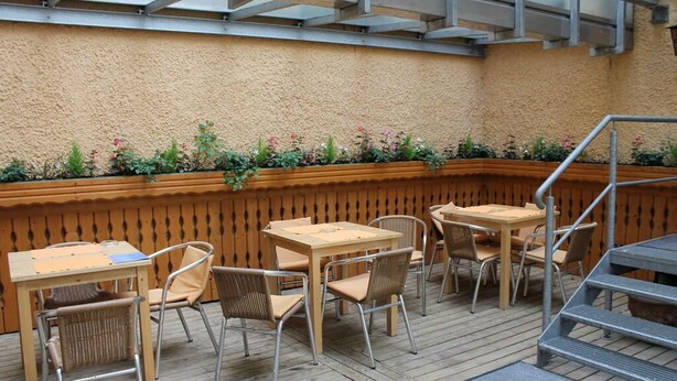 Une terrasse extérieure avec des tables et des chaises en bois, un banc en bois et un jardinier orné de fleurs.